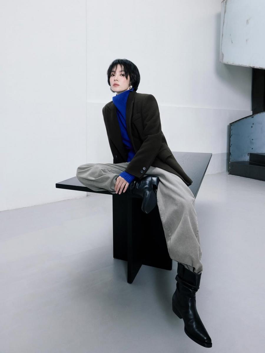 宋慧喬以深色大衣定錨整體氣場，下身搭配灰色休閒褲，透過正式與休閒材質的對比，讓造型顯得輕鬆卻不鬆散。寬褲的柔軟線條中和大衣的份量感，使整體輪廓更有流動性；尖頭短靴則點亮整體穿搭的層次感，為造型保留俐落重心。這樣的搭配不刻意顯年輕，卻因比例與材質拿捏得宜，自然流露出從容而有精神的減齡效果。