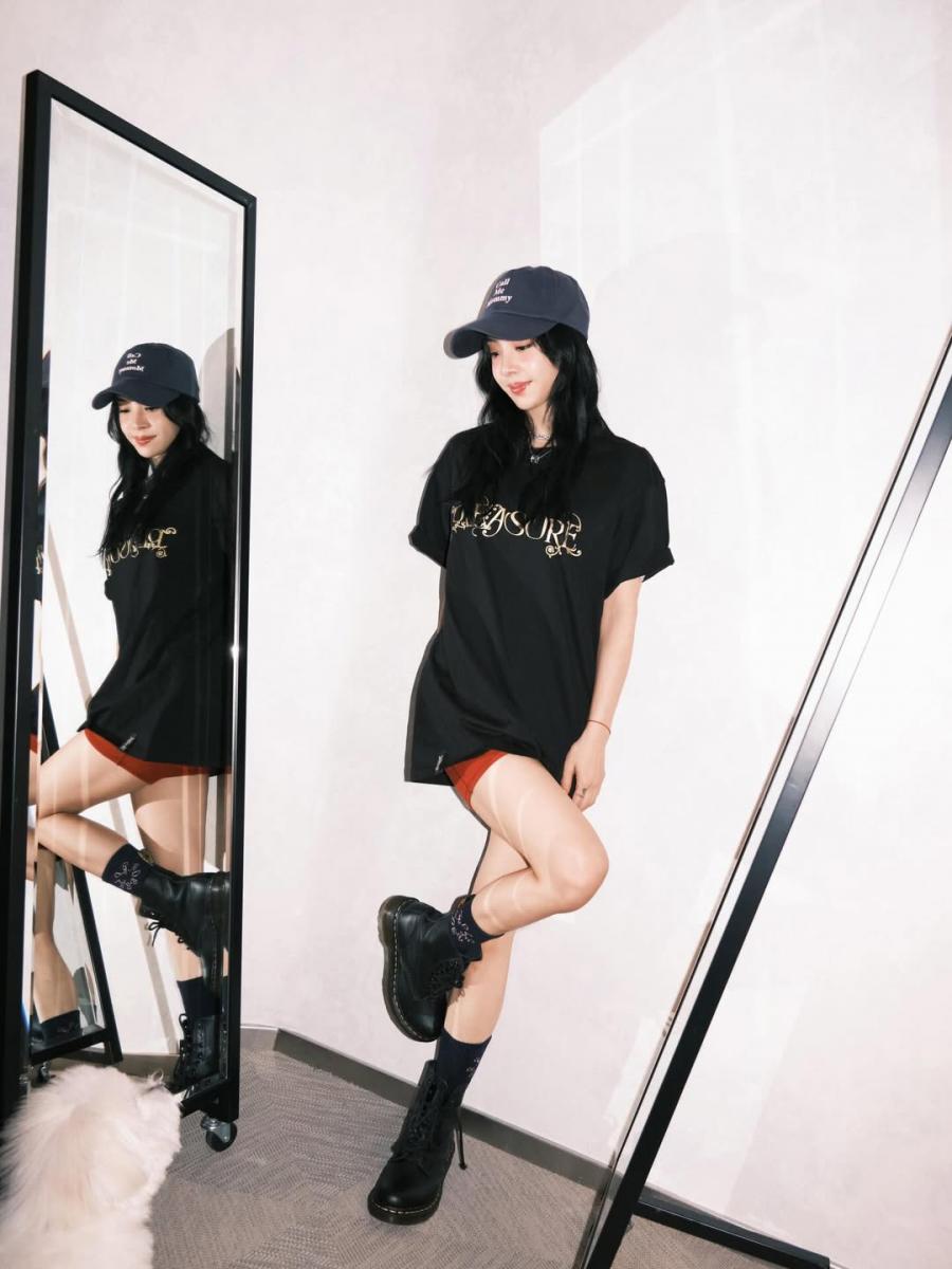 第一套造型看似簡單，卻是街頭風最不容易出錯的經典配置。寬鬆黑色T恤以「不貼身」的剪裁，保留身形線條的流動感，下身若隱若現的紅色單車褲，讓視覺重心自然往腿部延伸。棒球帽在這套造型裡不只是配件，而是整體風格的定錨點，讓休閒感更明確，也拉出年輕輪廓。腳上的馬汀靴則負責收尾，厚底與硬朗線條中和了T恤的隨性，讓整體看起來不是居家穿搭，而是有態度的街頭造型。這種「上寬下俐落」的組合，是街頭風穿搭裡最安全、也最顯精神的減齡關鍵。