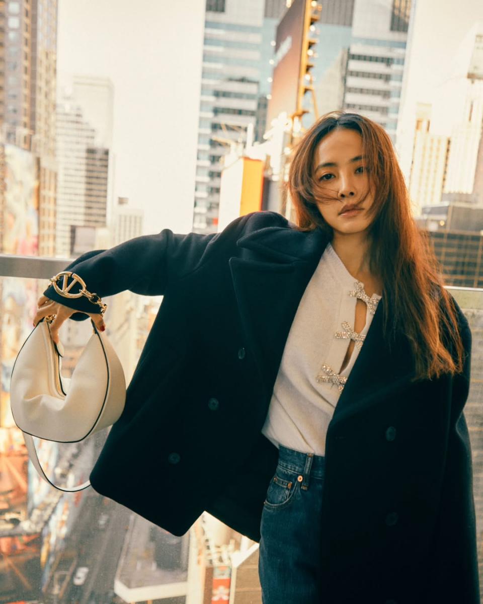 蔡依林這套穿搭的關鍵，在於用外套穩住比例，再把亮點集中在上半身。黑色短大衣長度俐落，不拖不壓，剛好停在臀線之上，讓腰線自然浮現；內搭的水鑽蝴蝶結針織衫，透過立體裝飾把視線往上拉，加上手提著的白色 Valentino VLogo Moon Bag，也為整體深色調加入精緻亮點。下身選擇高腰牛仔褲，線條筆直、不過度寬鬆，讓腿部比例被完整延伸。蔡依林刻意保留外套敞開的穿法，形成明確的縱向線條，即使搭配平實的丹寧單品，整體仍顯得修長俐落。這是一套非常適合小隻女孩冬日複製的穿法，不靠誇張剪裁，而是用短長對比與重心配置，穿出自然顯高的效果。
